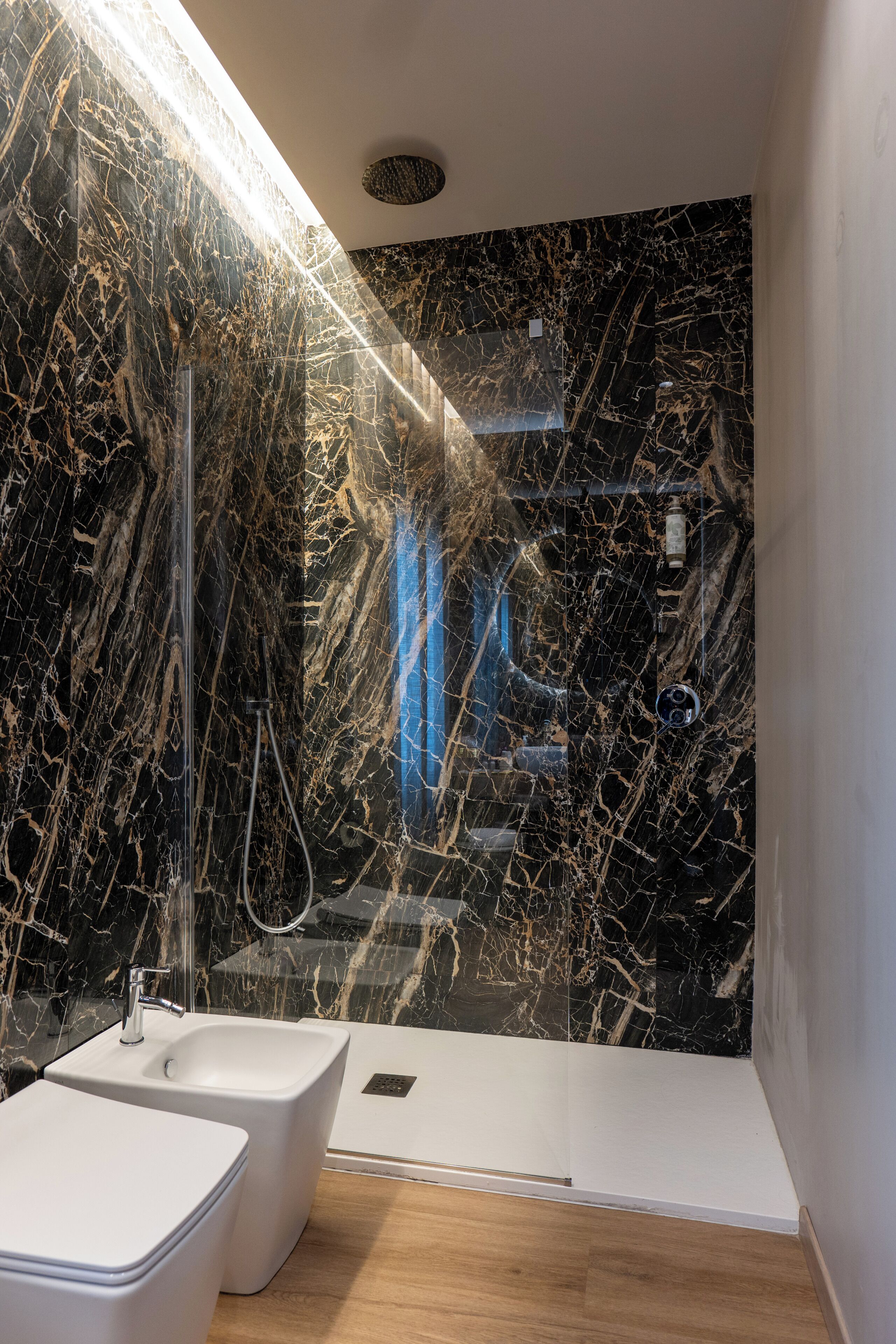 A modern bathroom with a black marble wall, a white sink, and a shower area.