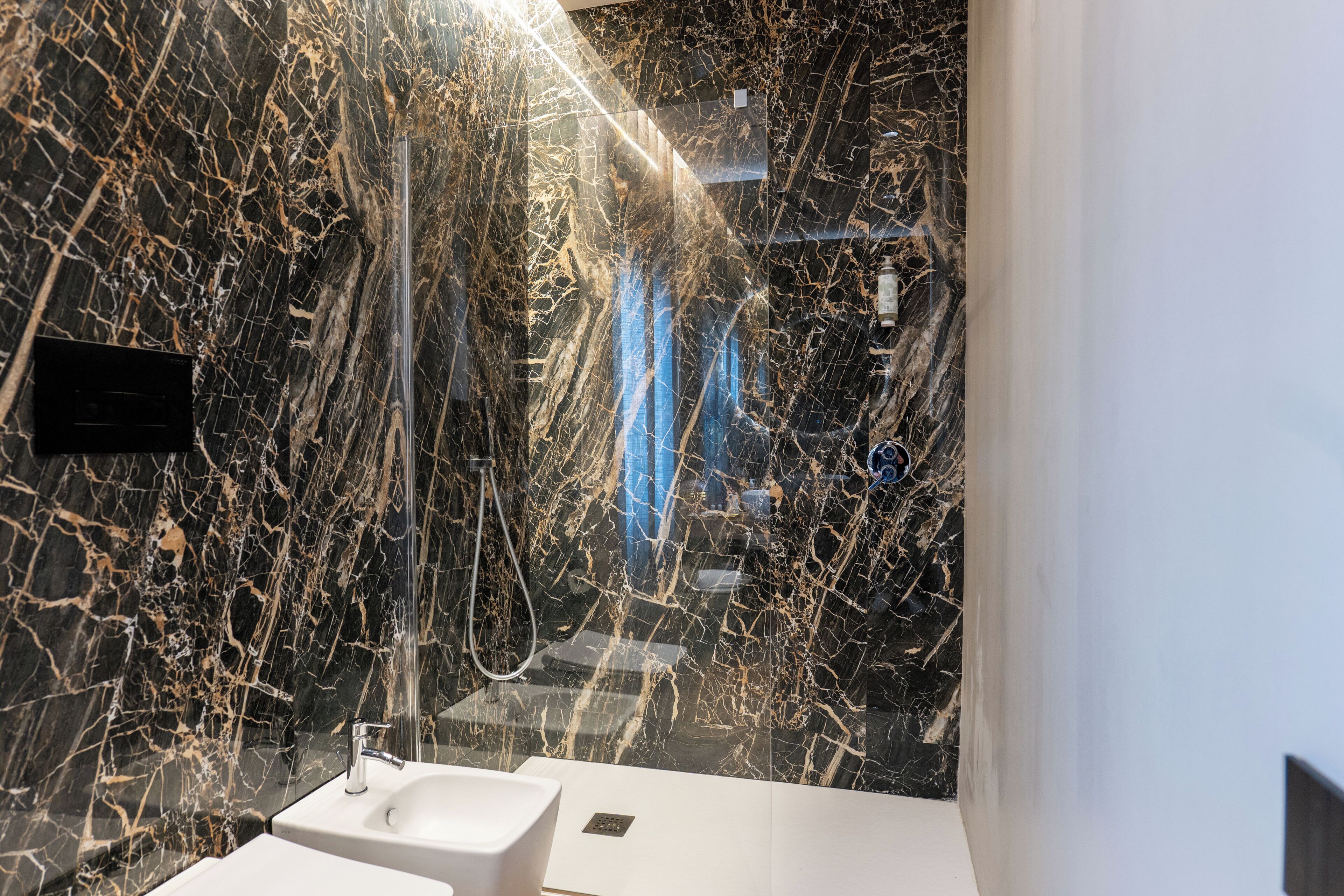 Un bagno moderno con una parete in marmo, un lavandino e una doccia.