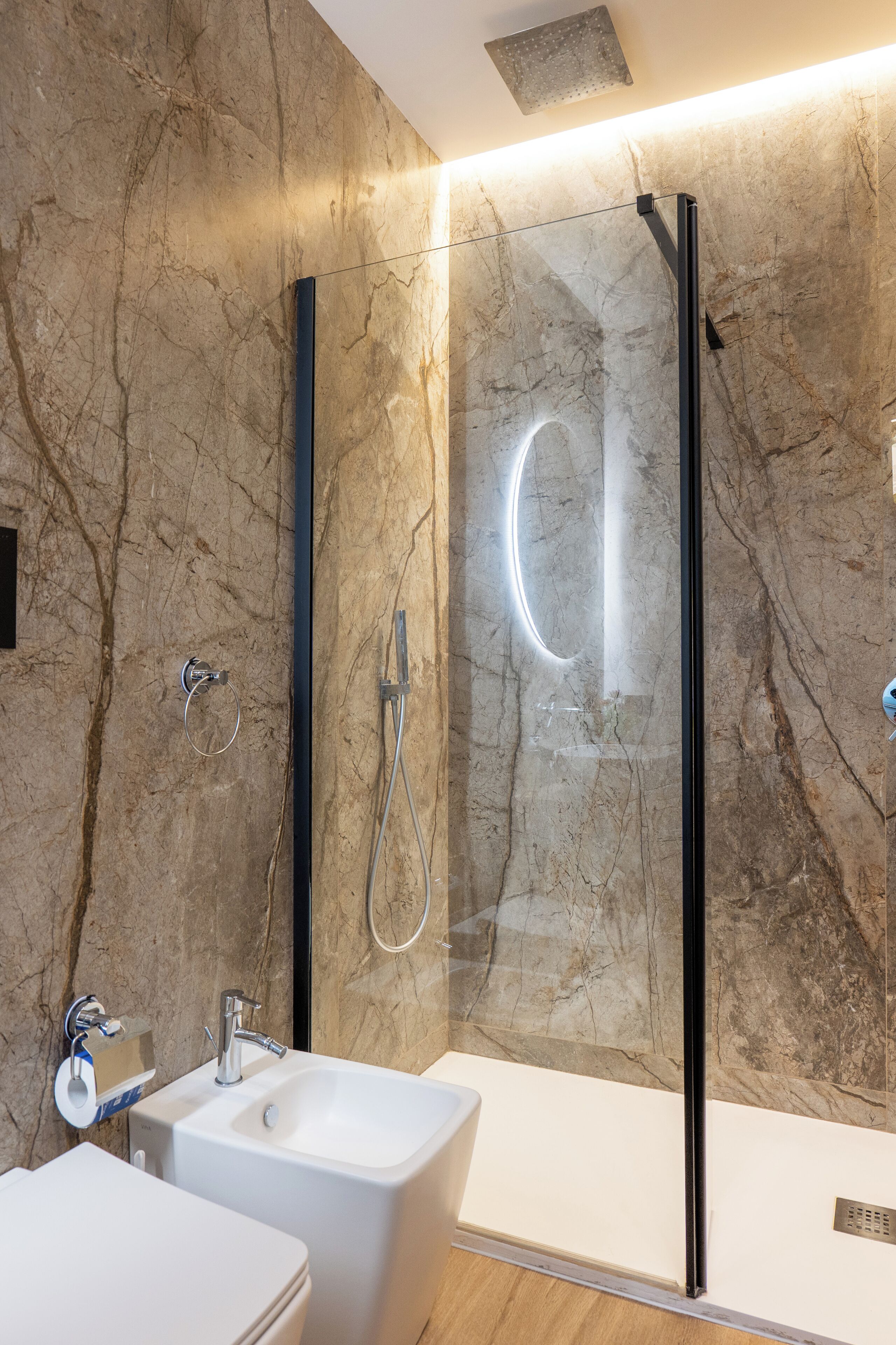 A modern bathroom with a glass-enclosed shower, a white sink, and a marble wall.