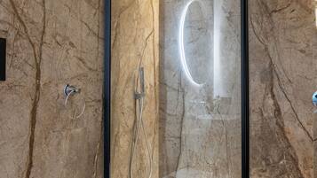 A modern bathroom with a glass-enclosed shower, a white sink, and a marble wall.