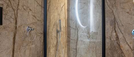 Une salle de bain moderne avec une douche à parois de verre, un lavabo blanc et un mur en marbre.