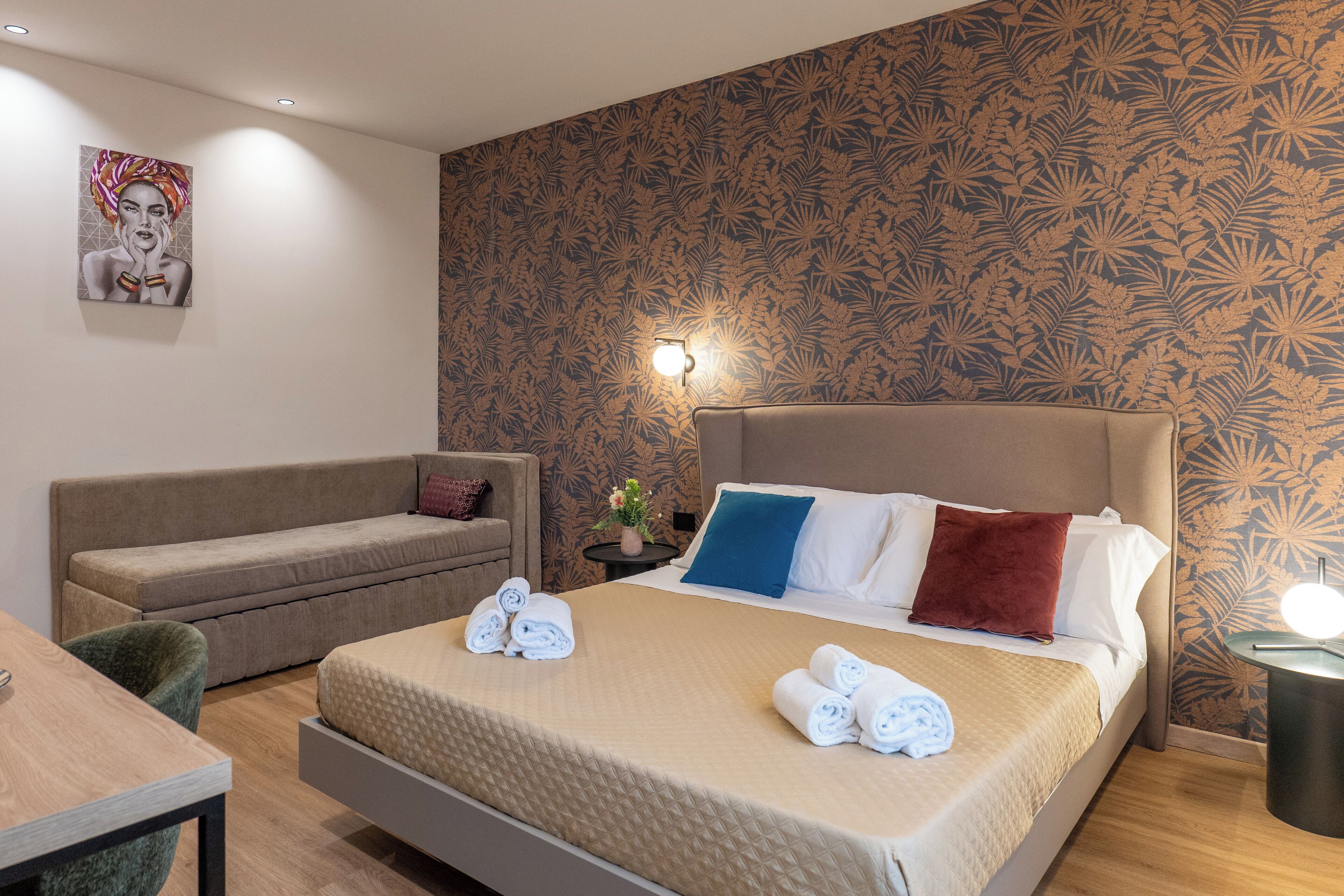 A hotel room with a bed, a sofa, a table, and a wall with a floral pattern.