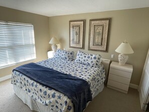 A bedroom with a bed, two bedside tables, a window with blinds, and wall-mounted lamps.