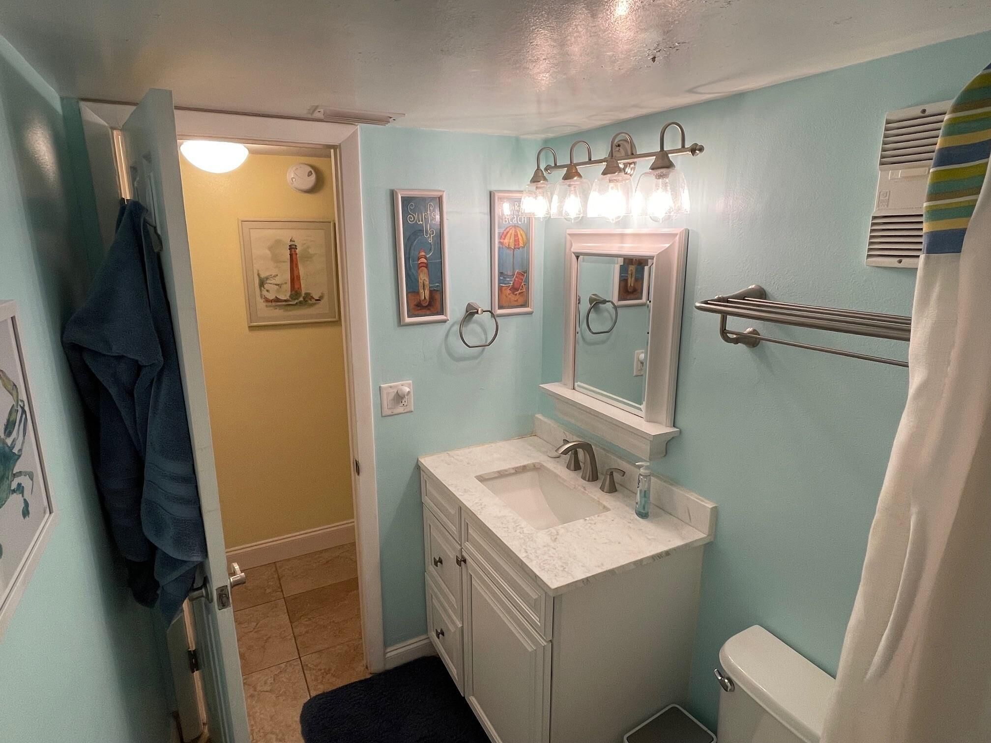 Une salle de bain équipée d’un lavabo, d’un miroir et de toilettes, avec des œuvres d’art accrochées aux murs et un porte-serviettes.