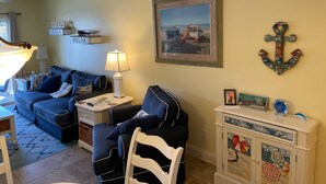 A living room with a sofa, a chair, a lamp, a framed picture, and a cabinet with decorative items.