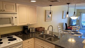 A kitchen with white cabinets, a stove, a sink, and a dining area with chairs.