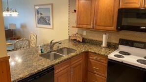 A kitchen with granite countertops, wooden cabinets, a stainless steel sink, a dishwasher, a stove, and a microwave. - Ocean View Second Floor 2/2 (New Smyrna Beach)