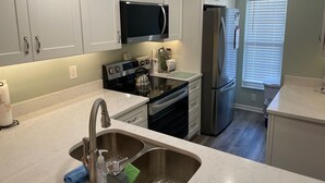 A modern kitchen with white cabinets, stainless steel appliances, a microwave, a refrigerator, and a sink with a faucet. - Ocean View  Second Floor 2/2 (New Smyrna Beach)