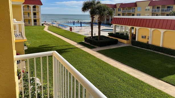 A hotel with a pool, green lawns, and a view of the ocean. - Ocean View  Second Floor 2/2 (New Smyrna Beach)