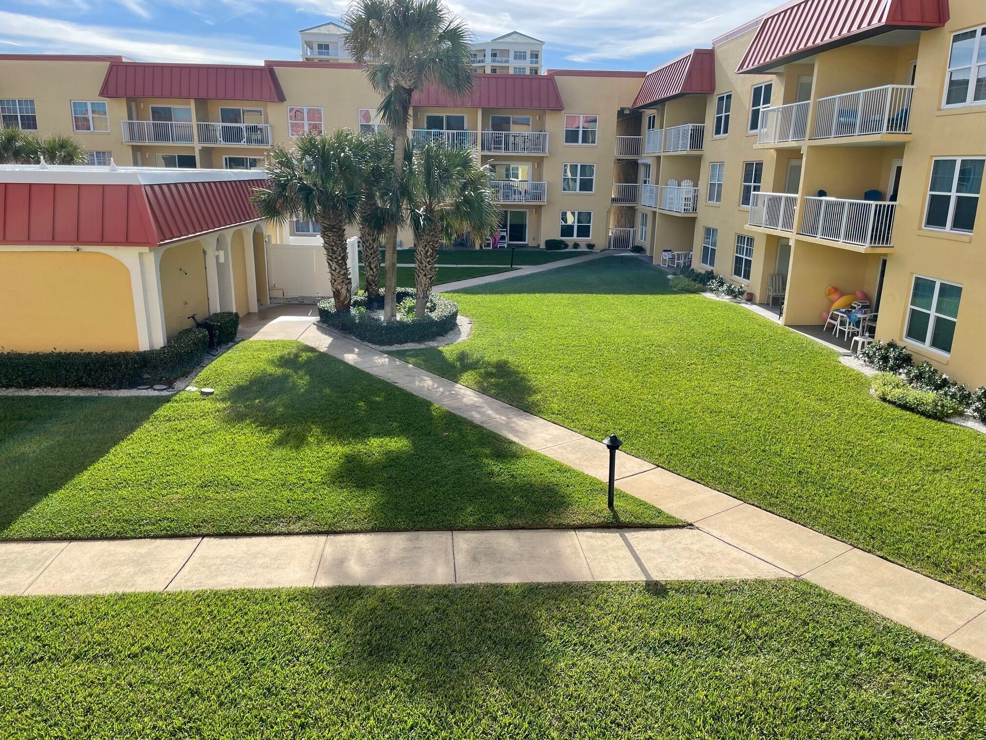 A courtyard with a well-maintained lawn, a central walkway, and a building with multiple balconies and windows.
