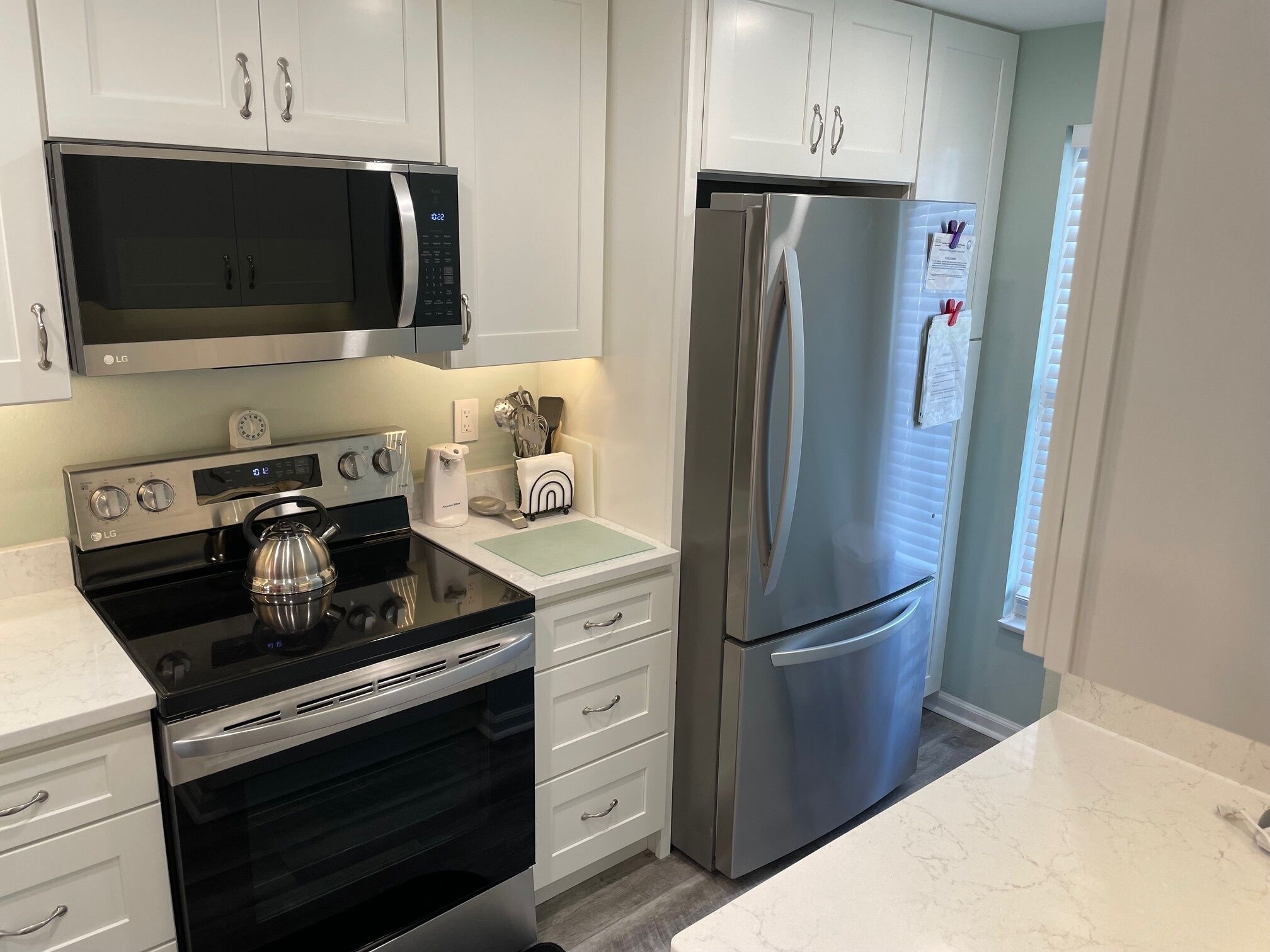 A modern kitchen with stainless steel appliances, white cabinetry, and a marble countertop.
