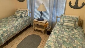 A room with two single beds, a nightstand with a lamp, and a window with curtains.