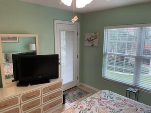 A bedroom with a television on a dresser, a door, a window with blinds, and a floral bedspread.