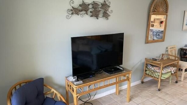 A living room with a television on a wooden stand, a blue cushioned chair, a small wooden table with a remote, and a decorative wall piece.
