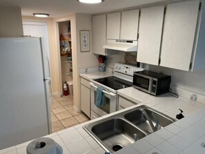 A compact kitchen with white cabinets, a refrigerator, a stove, a microwave, and a sink.