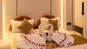 A hotel room with a bed featuring a heart-shaped towel arrangement and rose petals. - Parth Hotel (Ayodhya)