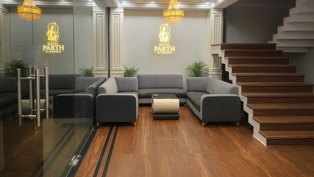 A modern hotel lobby with a grey sectional sofa, a wooden staircase, and two chandeliers. - Parth Hotel (Ayodhya)