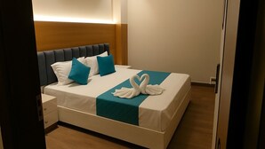 A neatly made bed with a teal bedspread and white pillows, a wooden headboard, and a bedside table with drawers. - Parth Hotel (Ayodhya)