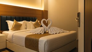 A neatly made bed with white linens, a dark headboard, and decorative swan-shaped pillows. - Parth Hotel (Ayodhya)