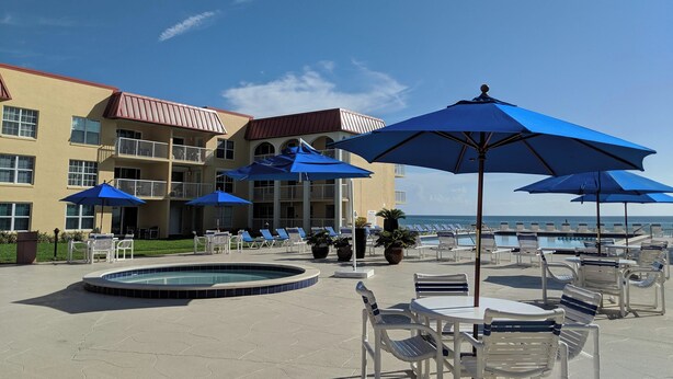 A hotel pool area with lounge chairs, umbrellas, and a swimming pool. - Ocean View Second Floor 2/2 (New Smyrna Beach)
