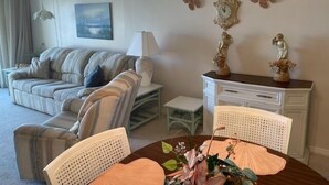 A living room with a sofa, two armchairs, a small table with a lamp, a decorative clock, and wall art. - Ocean View Second Floor 2/2 (New Smyrna Beach)
