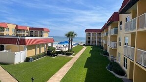 A hotel courtyard with a pool, a beach view, and a well-maintained lawn. - Ocean View Second Floor 2/2 (New Smyrna Beach)