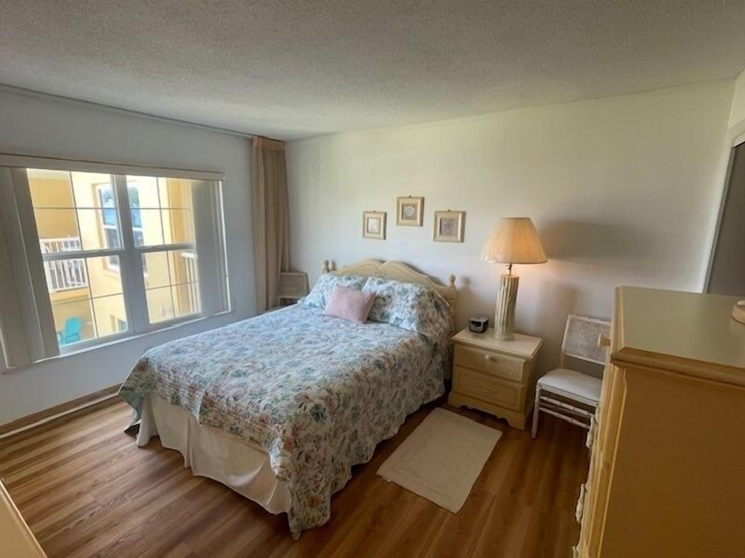 Un dormitorio con cama, mesitas de noche, lámpara, ventana y vistas a edificios.
