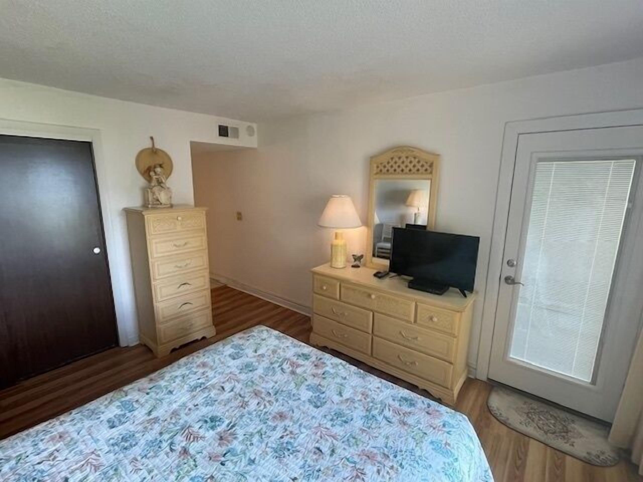 Une chambre à coucher avec un lit, une commode, un téléviseur et une porte.