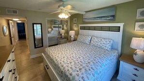 Un dormitorio con cama, mesitas de noche, ventilador de techo y un cuadro en la pared.