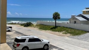 Un SUV blanco estacionado en un camino de entrada pavimentado, con vista al océano y una palmera al fondo.