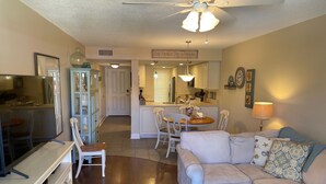 A cozy living room with a sofa, a coffee table, and a TV. There's a dining area with a table and chairs, and a kitchen in the background. - Ocean View Second Floor 2/2 (New Smyrna Beach)