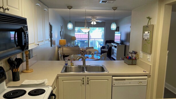A compact kitchen with a stove, sink, and dishwasher. There is a dining area with a table and chairs. - Ocean View Second Floor 2/2 (New Smyrna Beach)