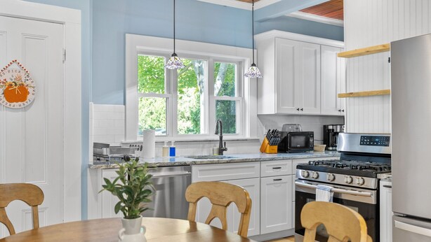Una cocina moderna con armarios blancos, un refrigerador de acero inoxidable, una estufa a gas y un microondas.