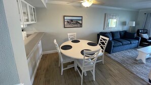 Un espacio habitable compacto con comedor que incluye una mesa redonda y sillas blancas, ventilador de techo y una pequeña cocina con armarios.