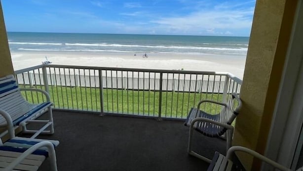Een balkon met uitzicht op het strand, twee ligstoelen en een hekwerk.