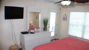 A bedroom with a bed, a dresser, a television mounted on the wall, and a door leading to another room.