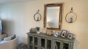 Una sala de estar con un sillón blanco curvo, un mueble de madera con puertas de cristal y un espejo grande encima.