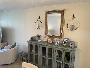 Un salon avec un fauteuil blanc aux lignes courbes, un meuble en bois doté de portes en verre et un grand miroir placé au-dessus.