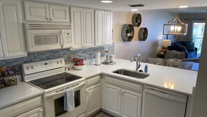 Una cocina moderna con armarios blancos, horno integrado, microondas, pileta y lavavajillas.