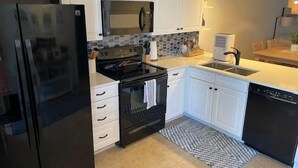 Une cuisine moderne avec des meubles blancs, un réfrigérateur noir, une cuisinière et un lave-vaisselle.