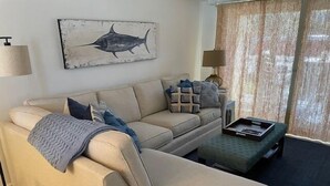 Un salon avec un canapé beige, une table basse et une œuvre d’art représentant un poisson, accrochée au mur.