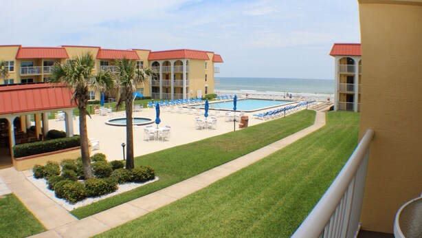 Un hotel con zona de piscina, palmeras y vistas a la playa.