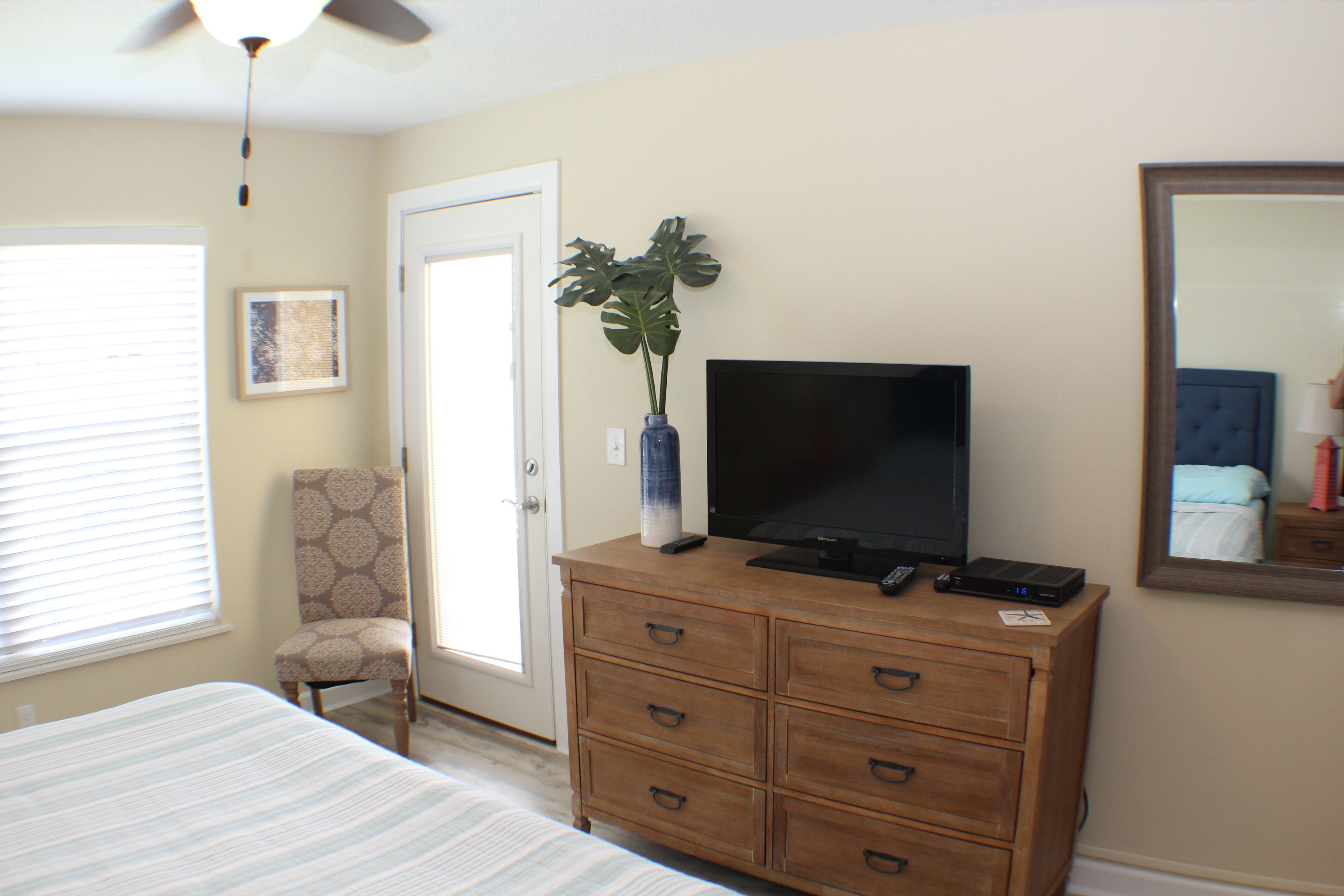 A bedroom with a bed, a dresser, a television, a chair, and a door.