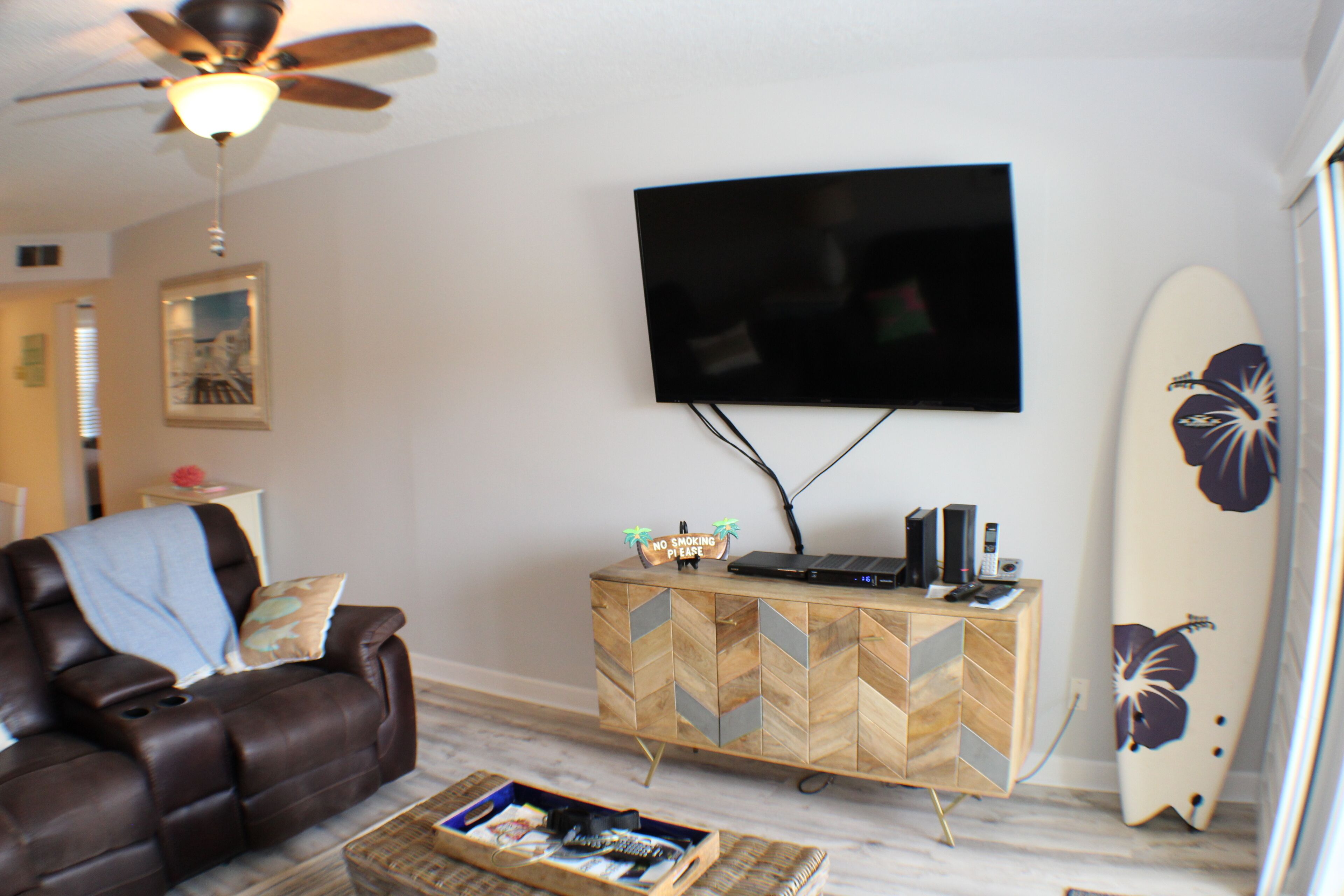 Ein Wohnzimmer mit Ledersofa, einer Holz-Unterhaltungsanlage, einem an der Wand befestigten Flachbildfernseher und einem Surfbrett.
