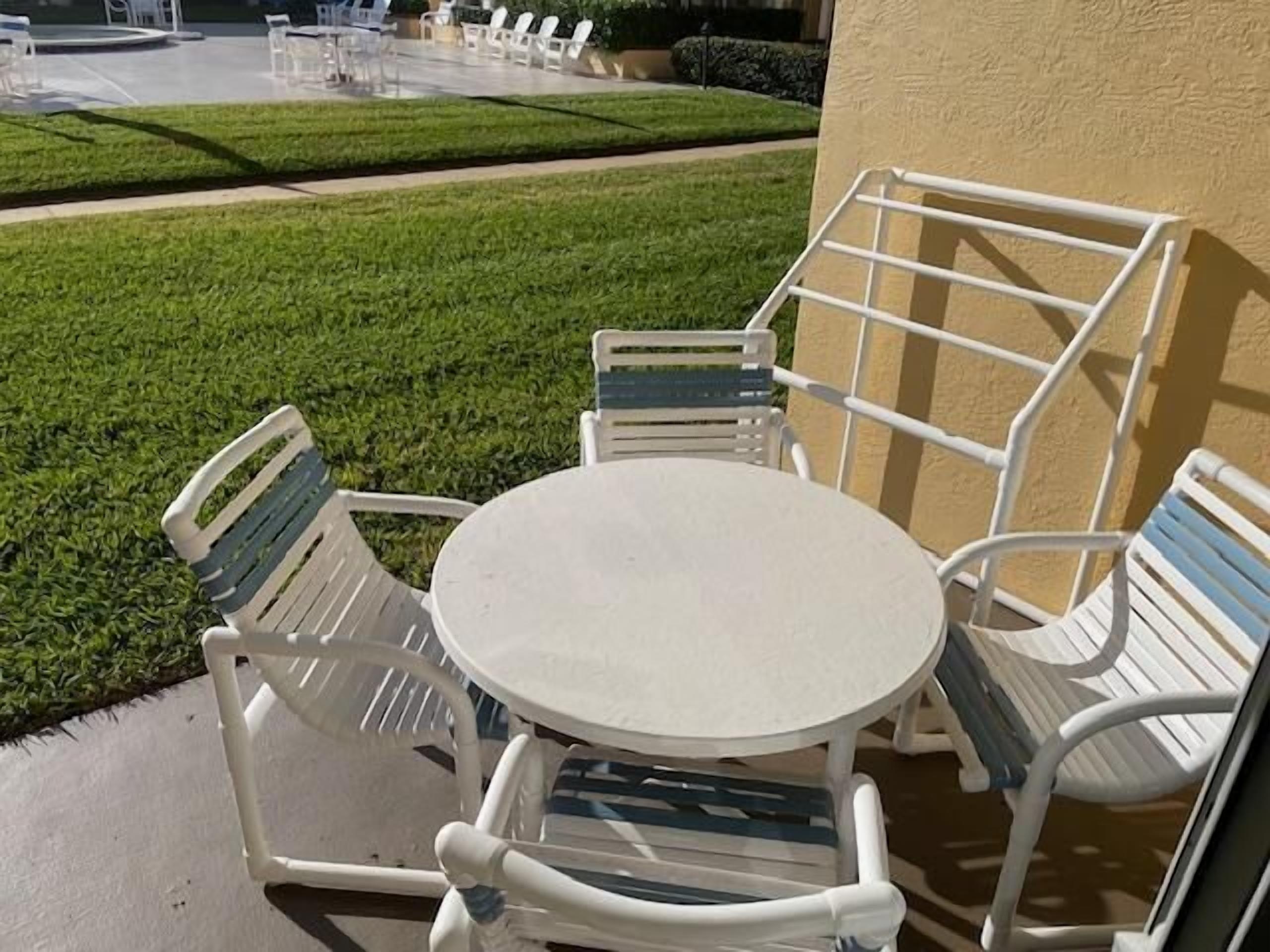 Een terras met een ronde tafel en vier stoelen, omgeven door een verzorgd gazon en een gevel.