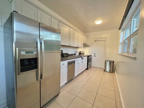 A modern kitchen with stainless steel appliances, white cabinetry, and a tiled floor.