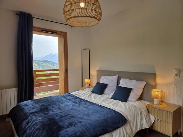 A bedroom with a bed, bedside lamps, a wooden nightstand, a window with a view of mountains, and a wicker ceiling light.