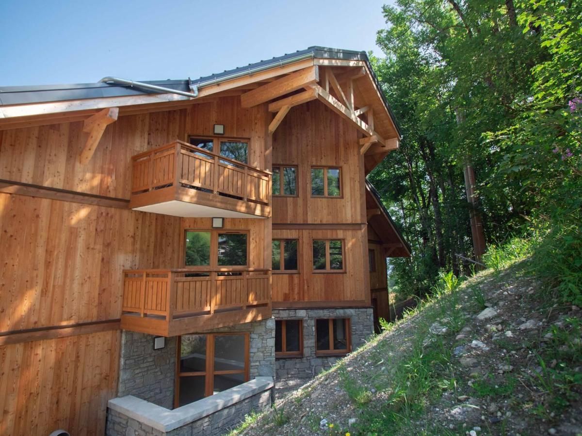 Een houten chalet met meerdere verdiepingen, balkons en grote ramen, omgeven door bomen.