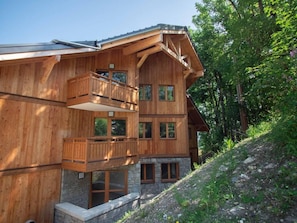A multi-story wooden chalet with balconies and large windows, surrounded by trees.