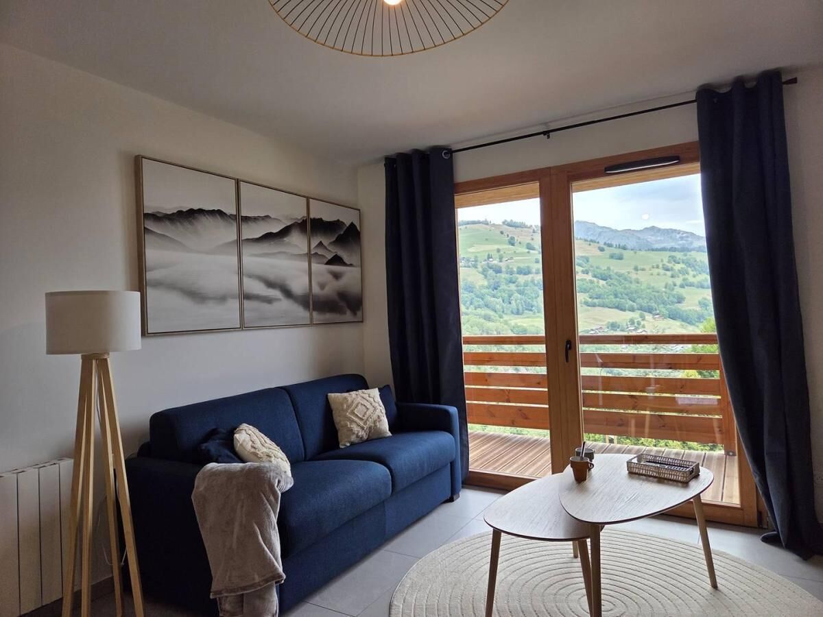 A modern living room with a blue sofa, a floor lamp, a table, and a large window with a view of a green landscape.
